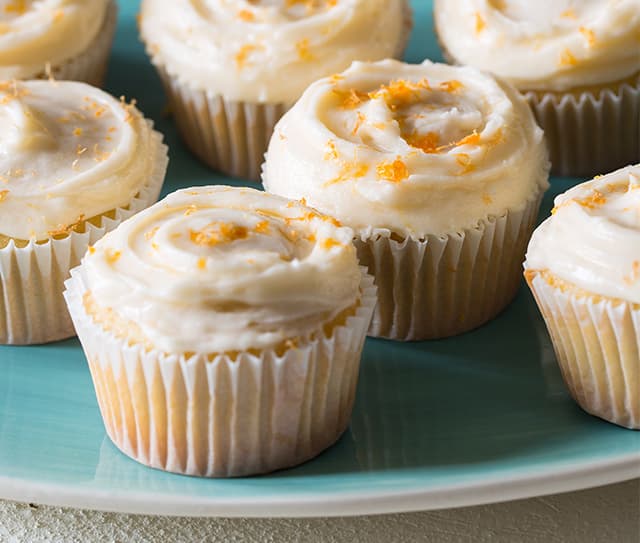 Tray full of butter cupcakes with grapefruit buttercream frosting and orange zest