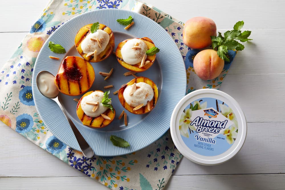 Plate full of grilled peaches topped with Almond Breeze Vanilla Almondmilk Yogurt